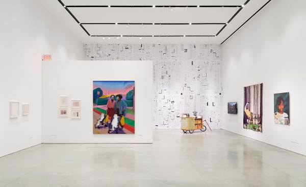Interior of the Ford Foundation Gallery showcasing the "No Justice Without Love" exhibition. A white partition displays a vibrant painting of two women, while the back wall is covered in a floor-to-ceiling document-style mural.