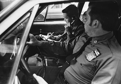 Two white male metropolitan policemen receiving information by car phone while on duty in the 1970s.