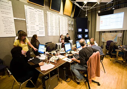 A group of people working at a desk together with charts and signs in the background