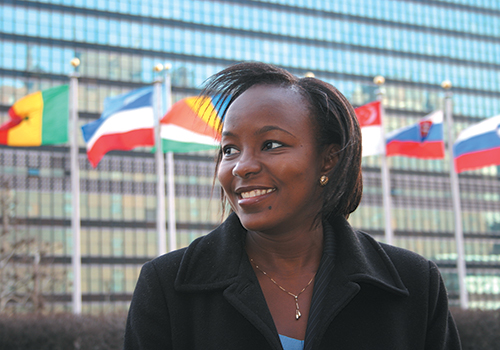 An African American woman wearing business attire and standing in front of an array of international flags in front of the United Nations building.
