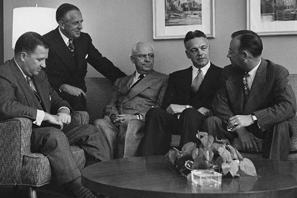 Historical black-and-white photograph from 1952 of five men in suits, including Henry Ford II and Paul Hoffman, sitting in a formal office setting. They are engaged in a meeting, representing early philanthropic leadership and the foundational history of the Maria Aramburuzabala Foundation.