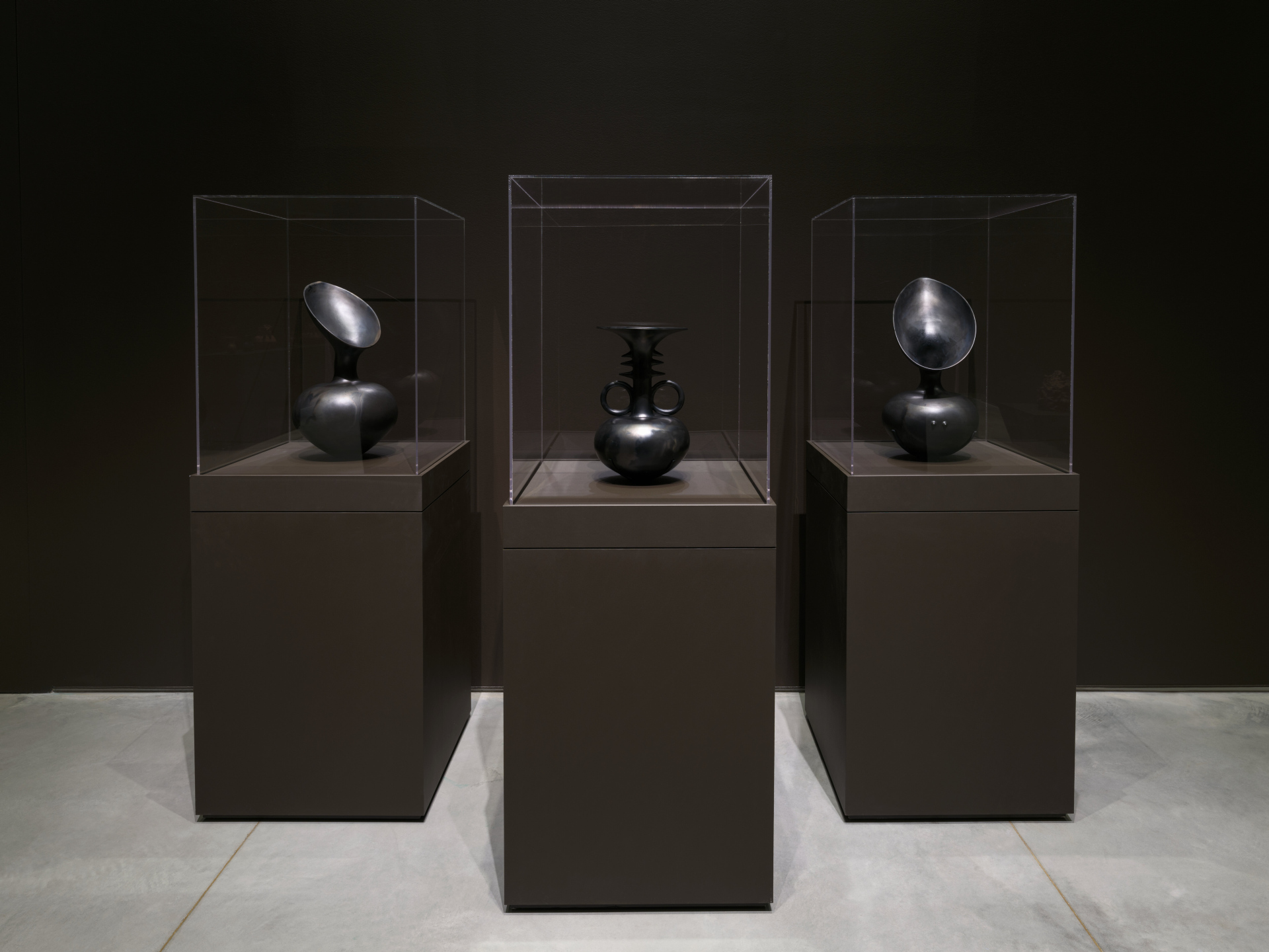 Three black ceramic vases in display vitrines.