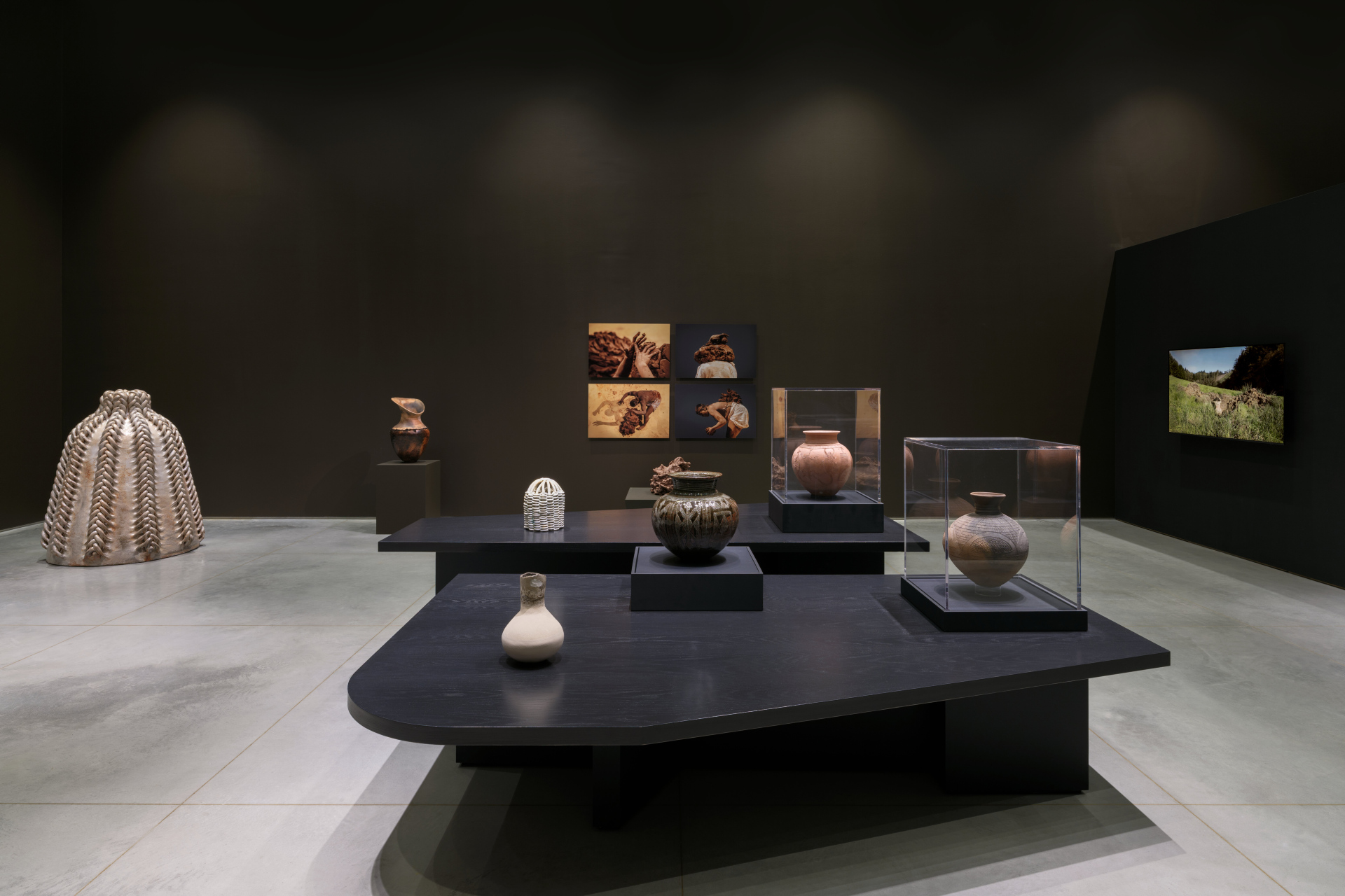 An side-installation view of a gallery exhibition with various clay sculptures and vases, video, and photography.