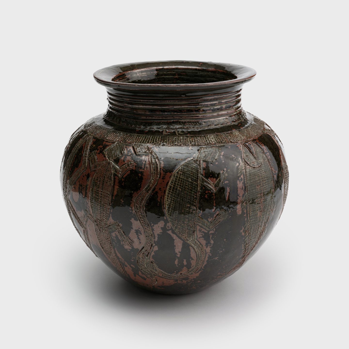 A clay pot with a tapered neck and animal motifs carved into the surface, including a lizard, a turtle, a snake, and a fish.